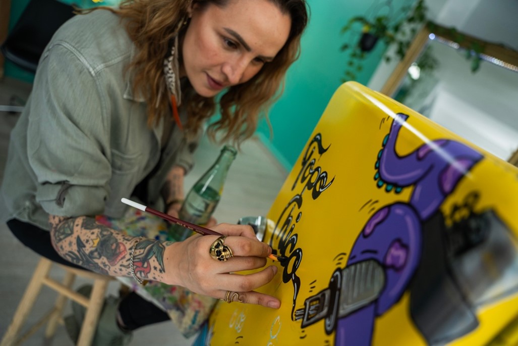 Diseñadora pintando en una heladera Topo Chico de color amarillo con un pulpo violeta