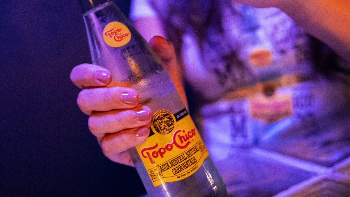 Botella de Topo Chico agua, con plato de comida y hielera Topo Chico.