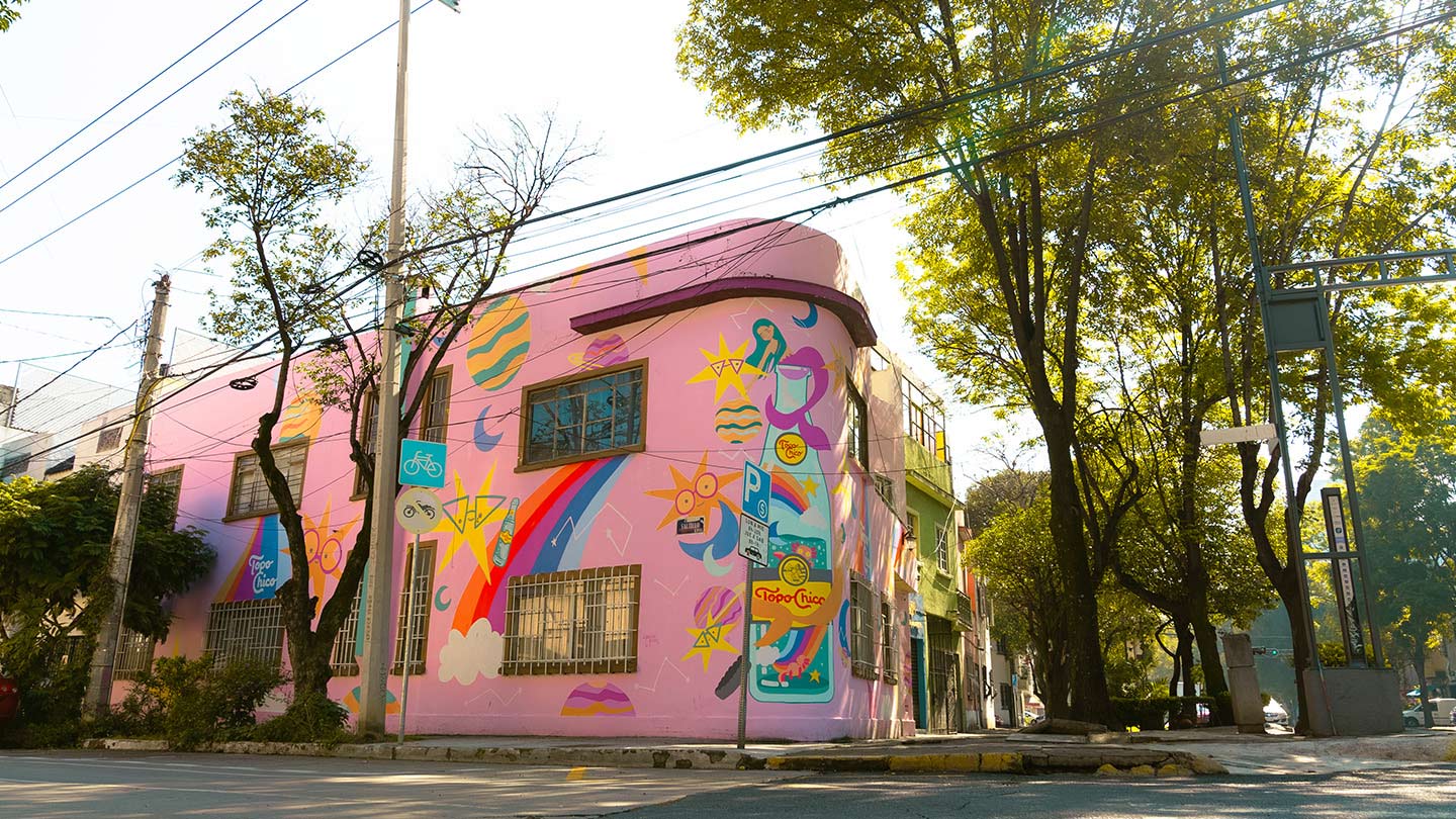 esquina de una casa de color rosa con dibujos de colores y una botella de Topo Chico pintada