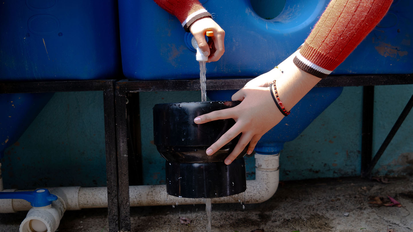 Unas manos cargando agua en un recipiento negro.