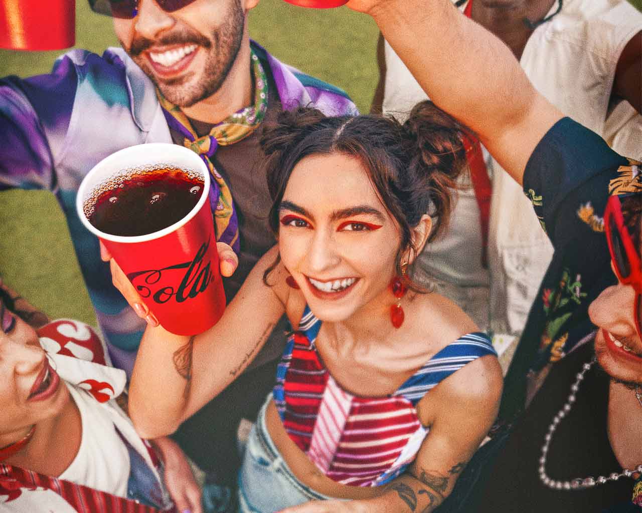 Joven levantando un vaso de Coca-Cola en una fiesta.