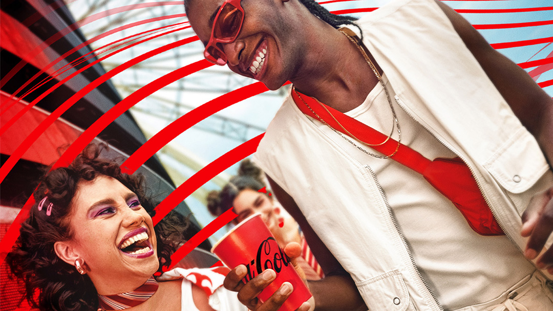 Dos personas riendo y disfrutando de Coca-Cola en un evento al aire libre.