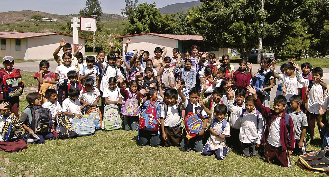 Niños saludan a cámara, en el patio de su escuela