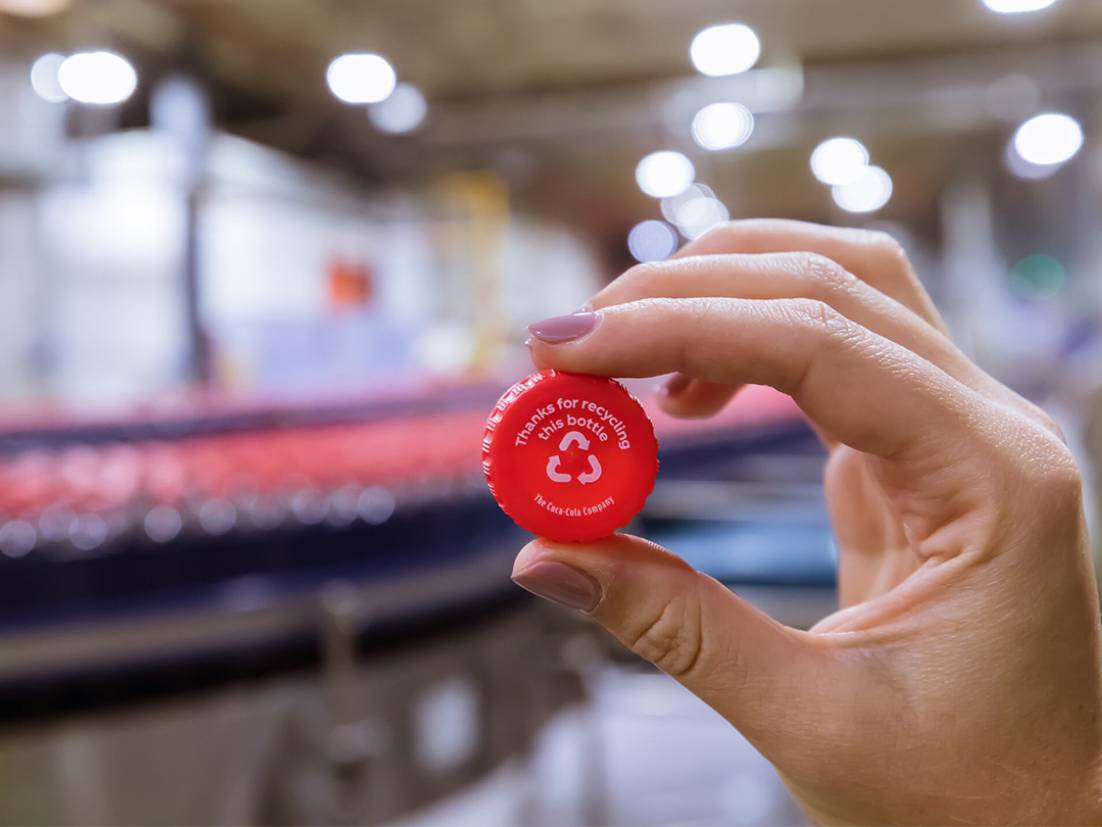 Detail of a person throwing a plastic bottle in Coca-Cola themed trash bin