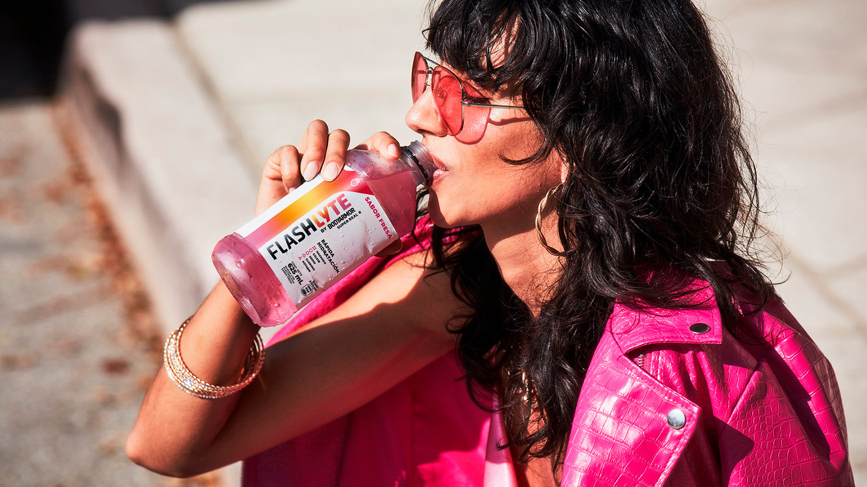 Mujer joven con un abrigo y gafas de color rosa, bebe una Flashlyte sabor fresa.