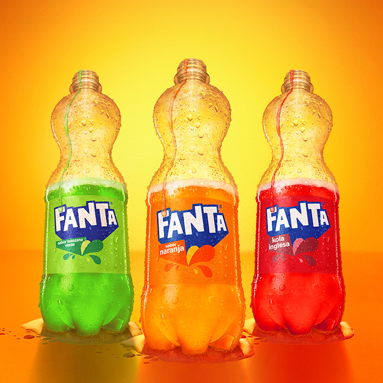 Botellas destapadas de Fanta sabor Naranja, Manzana Verde y Kola Inglesa sobre un fondo de color naranja.