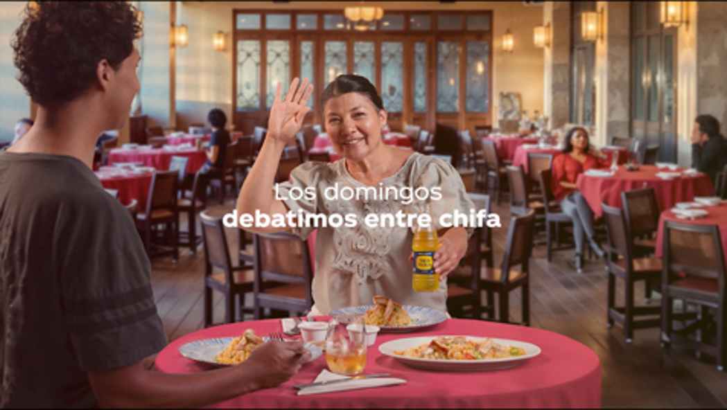 Una mujer y un joven sentados juntos en una mesa almorzando en un restaurant. Sobre la mesa hay dos botellas de Inca-Kola. Sobre la imagen, el título: "Los domingos debatimos entre chifa"