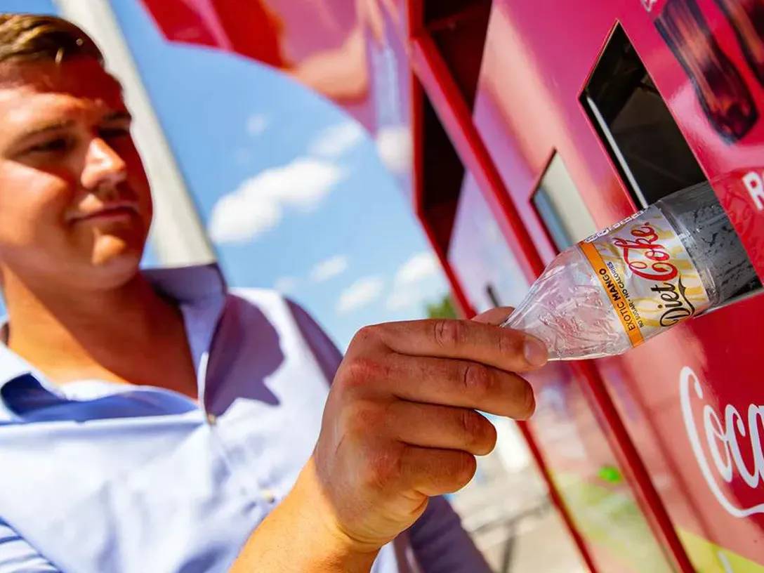 Detail of a man putting an empty Coca-Cola plastic bottle in a recyclable trash bin.