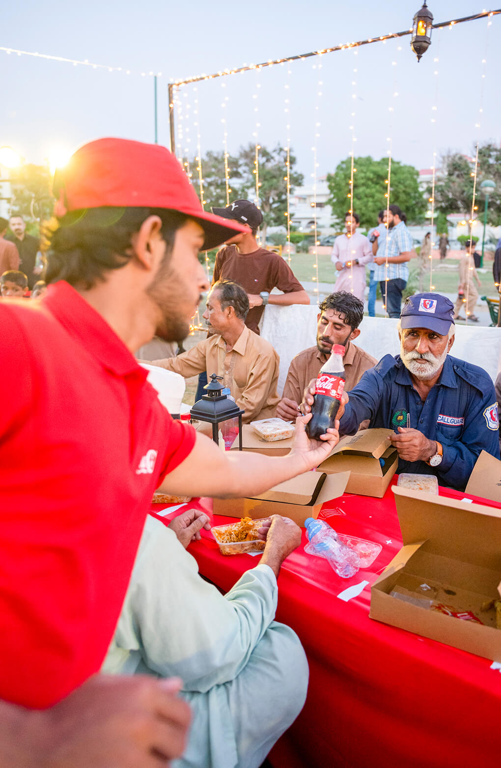 کوکا کولا کی وردی میں ملبوس شخص اپنے سامنے میز پر بیٹھے شخص کو کوکا کولا کی بوتل دے رہا ہے۔