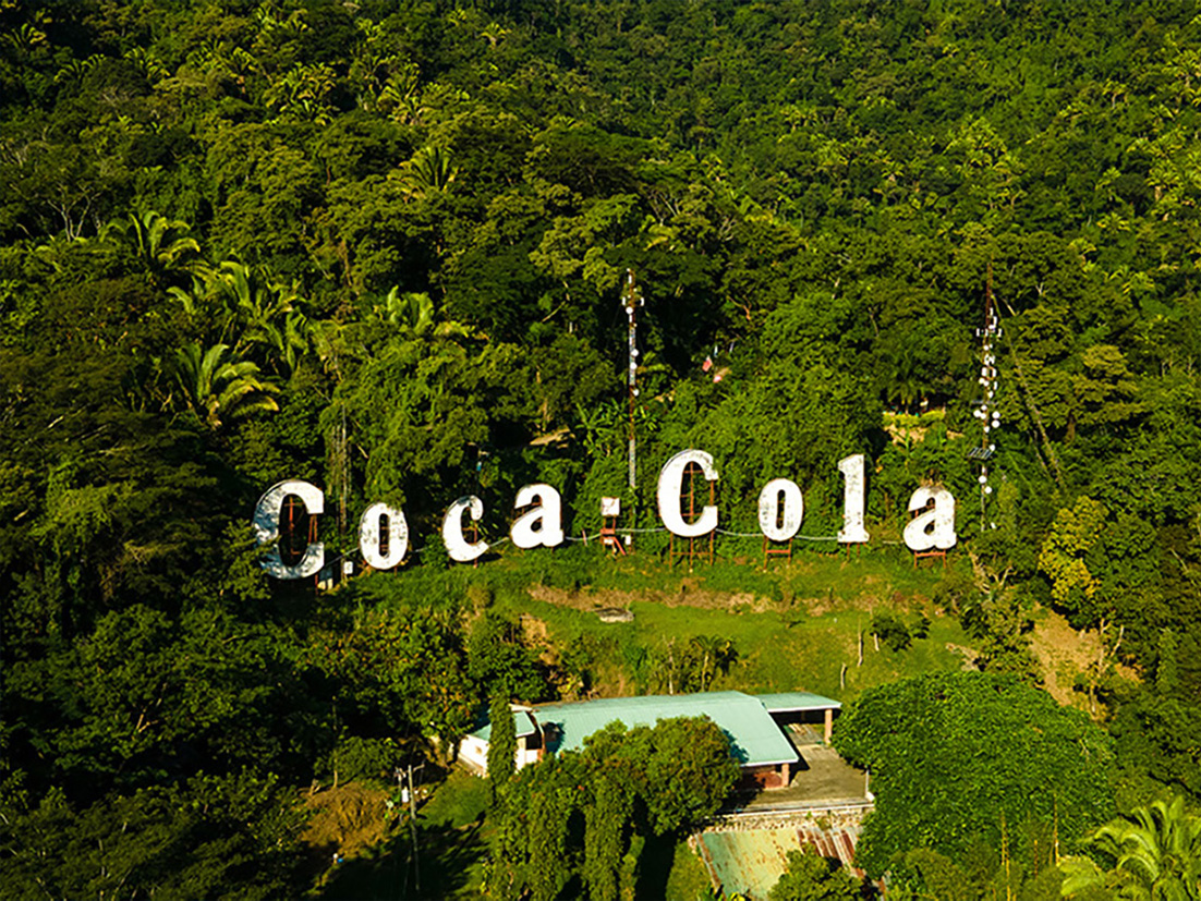 Paisaje de un bosque visto desde el aire con un cartel de Coca-Cola blanco.