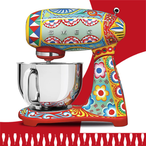 Barevný kuchyňský robot Smeg s nerezovou miskou a výrazným vzorovaným designem na červeném a bílém pozadí.