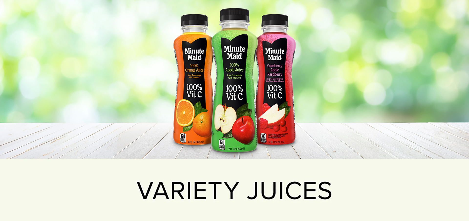 The same three Minute Maid bottles (100% Orange Juice, 100% Apple Juice, and Cranberry Apple Raspberry) standing on a white wooden table against a blurred green outdoor background, with "VARIETY JUICES" text below.