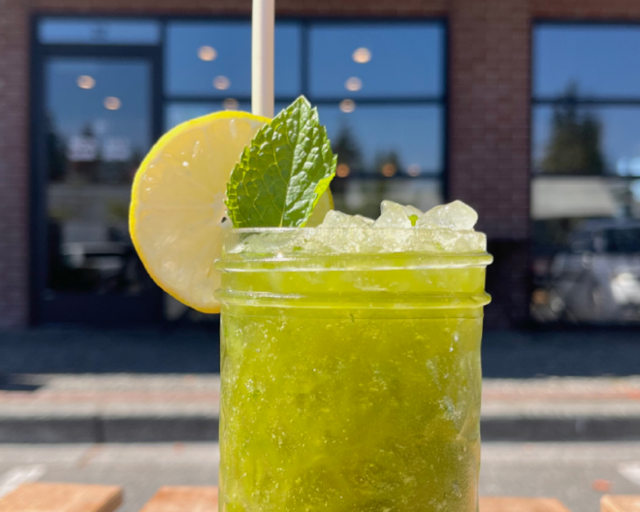 Yellow green drink in glass with ice and garnished with lemon wedge and mint leaf