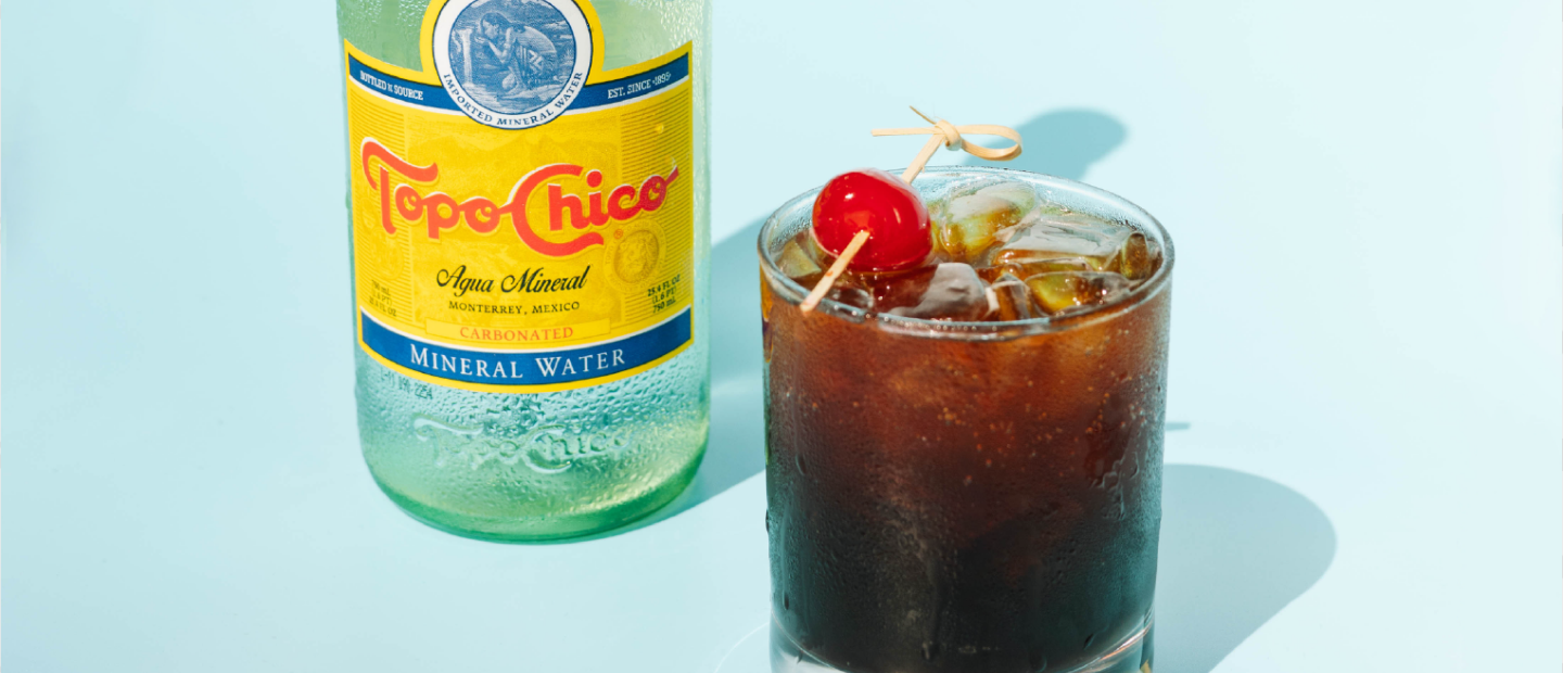 A cherry sproda glass next to a Topo-Chico bottle