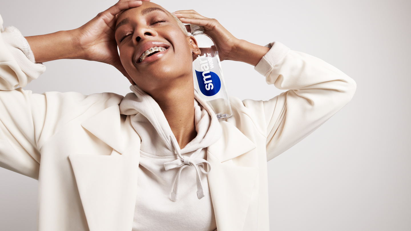 Smiling woman holding a Glacéau Smartwater bottle next to her head