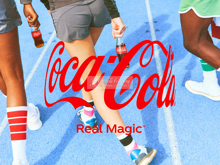 Close-up of people's legs walking on a blue running track, some holding Coca-Cola bottles, with a large red Coca-Cola logo and the tagline 'Real Magic' overlaid on the image