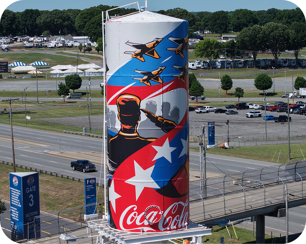 Close-up of Amber Thompson's Coca‑Cola mural on a water tower, showing jets and a saluting figure.