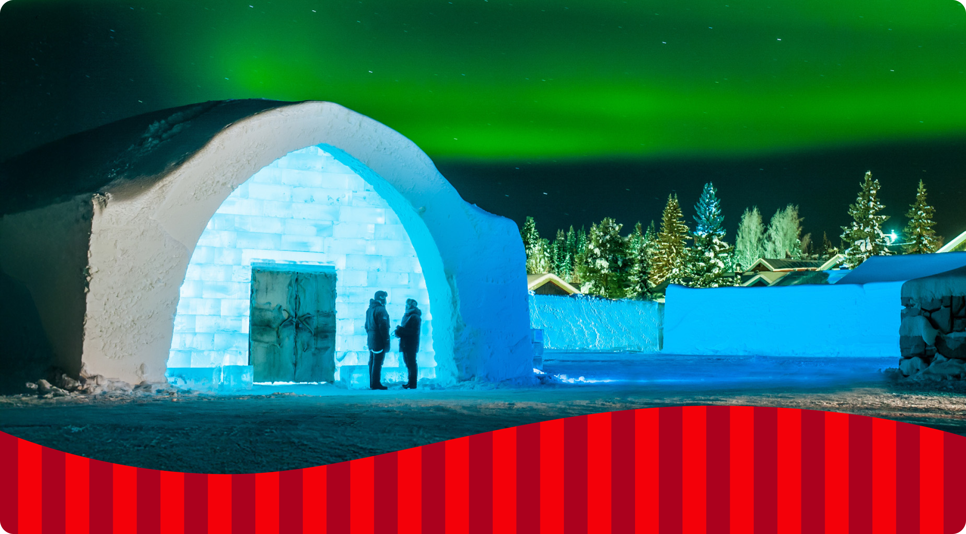 Two people standing and talking outside of an igloo under the northern lights