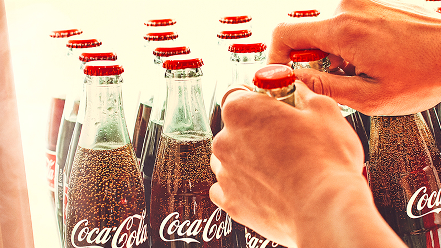 Manos tomando Coca-Colas de una heladera