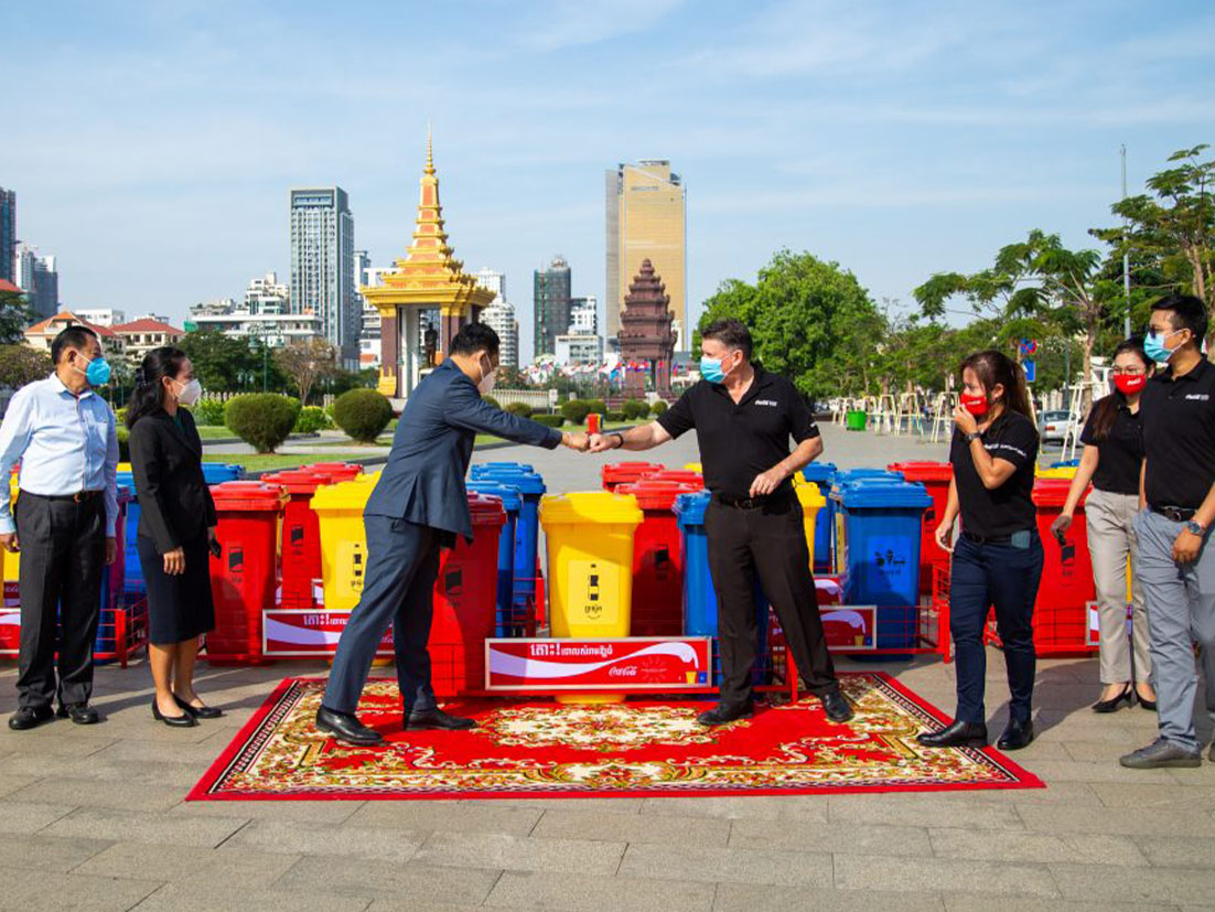 A group of people in front of several recyclable trash bins