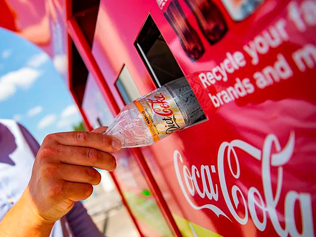 A man putting an empty Coca-Cola plastic bottle in a recyclable Coca-Cola bin